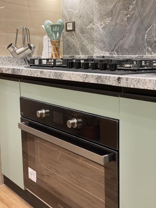 Built-in oven in sage green cabinetry under a granite worktop