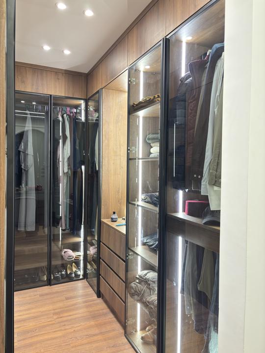 Walk-in dressing room with lit glass-door wardrobes in walnut