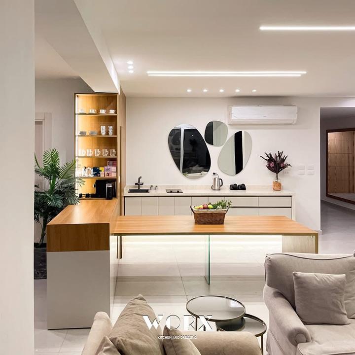 Open-plan kitchenette with oak bar table and lit shelving