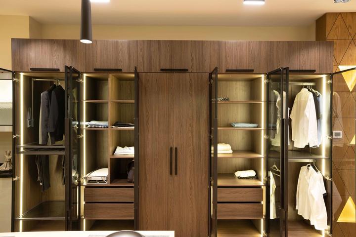 Walnut wardrobe wall with lit glass doors, shelves and hanging rails